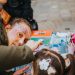A face painter artistically decorates a child's face outdoors at a vibrant street festival.